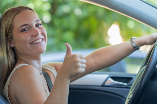 Happy young woman giving thumbs up while sitting in driver's seat of car, smiling confidently with hand on steering wheel, new driver success concept