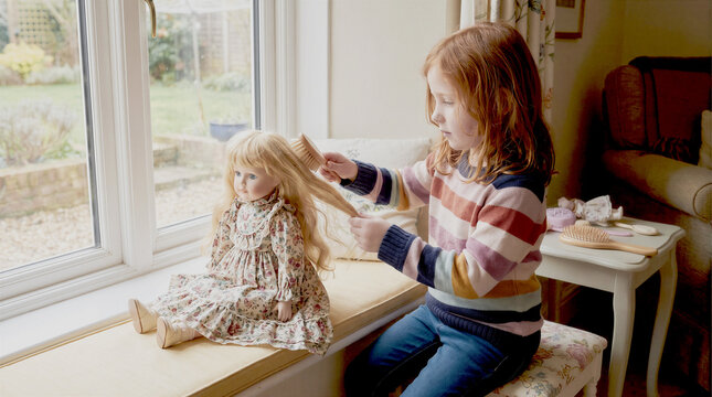 Little girl brushing hair of her favorite doll indoors