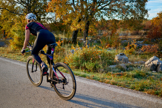 Female Cyclist Training On Road Bike Through Scenic Autumn Countryside At Sunrise