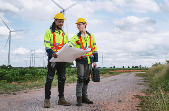 Two workers stand on a dirt path near wind turbines
