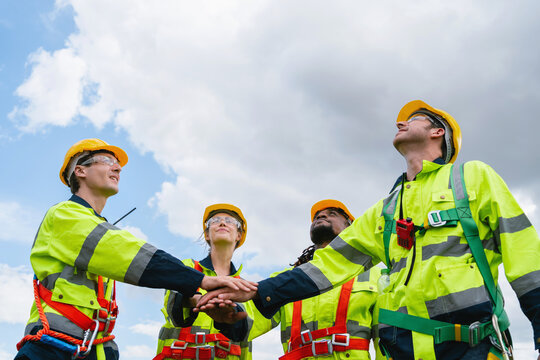 Four workers in safety gear high-five outdoors