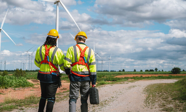Two engineers walk toward wind turbines under a partly cloudy sky