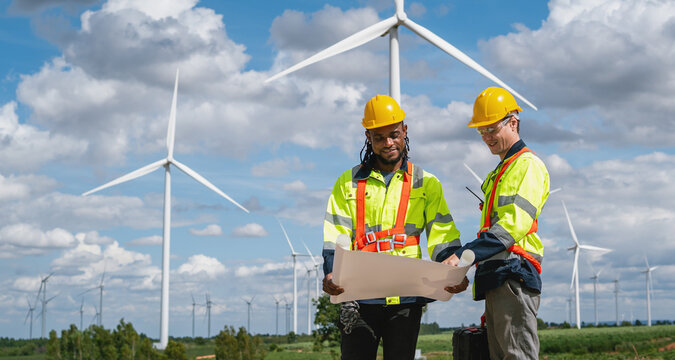 Two engineers review plans under wind turbines