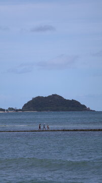 The image depicts a tranquil seascape with a small group of four people walking along a narrow strip of land that extends into the water, seemingly a sandbar or a beach