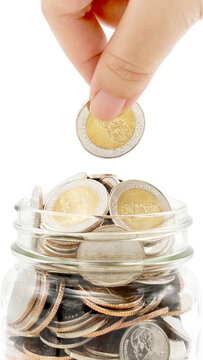Woman's hand dropping ten Thai Baht coin into a glass jar full of coins. Business and finance concept. Vertical Photography.