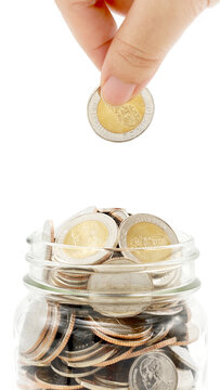 Woman's hand dropping ten Thai Baht coin into a glass jar full of coins. Business and finance concept. Vertical Photography.