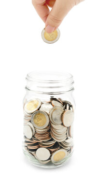 Woman's hand dropping ten Thai Baht coin into a glass jar full of coins. Business and finance concept. Vertical Photography.
