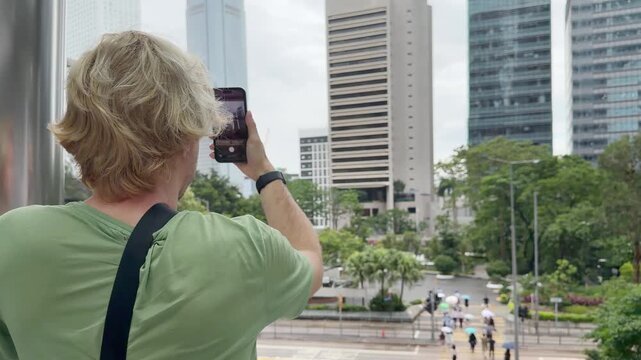 Young Blond Man Using Smartphone on City Street with Skyscrapers Background 