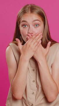 I will not say anything. Frightened woman closing mouth with hands, looking intimidated scared at camera, gestures no, refusing to tell terrible secret, unbelievable truth. Lady on pink background