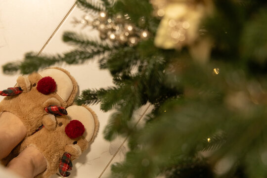 Festive slippers on a white floor beside a Christmas tree decorated with ornaments