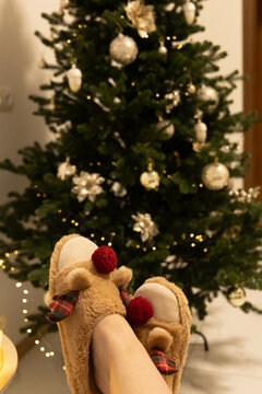 Cozy feet in reindeer slippers in front of a decorated Christmas tree during the holiday season