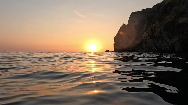 Vibrant sunset glowing over calm sea waves near dramatic rocky cliffs. Low angle tracking shot.