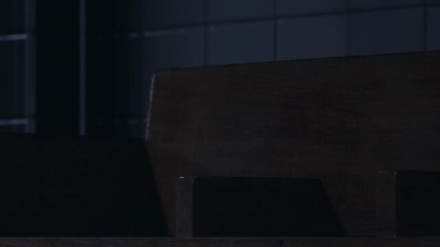 A wooden bench stands quietly in a corner of a dimly lit room. The low light creates shadows, highlighting the simple design. Evening light adds to the atmosphere of the space.