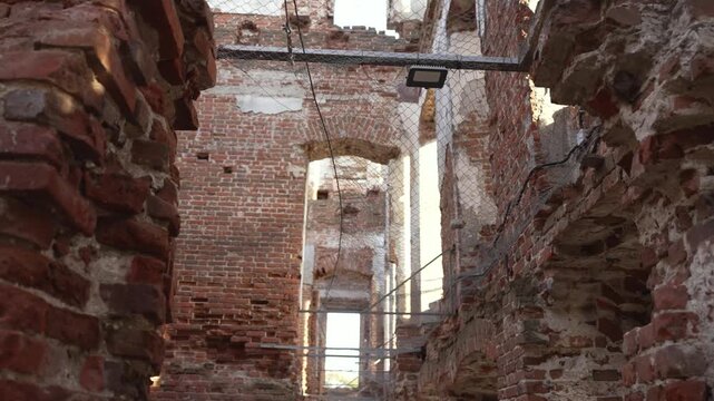 Video pans through crumbling brick ruins with sunlight filtering through broken walls and arches. Metal scaffolding and wire mesh suggest preservation work. Atmosphere is quiet and historical