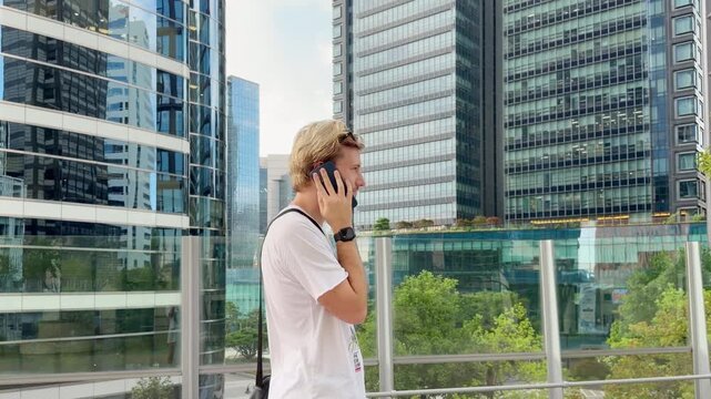Young Blond Man Standing on Bridge with Smartphone and Skyscraper Skyline in Background &ndash; Summer Day in Modern City