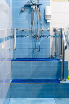 Accessible blue‑tiled shower area with steps, grab bars, handheld showerhead, and safety features