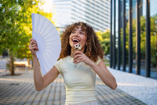 Happy woman enjoying ice cream and hand fan on summer day