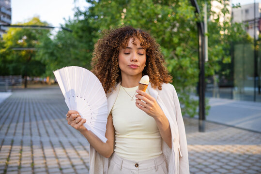 Woman cooling off with ice cream and fan on a hot summer day