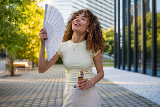 Woman enjoying ice cream and hand fan on hot summer day