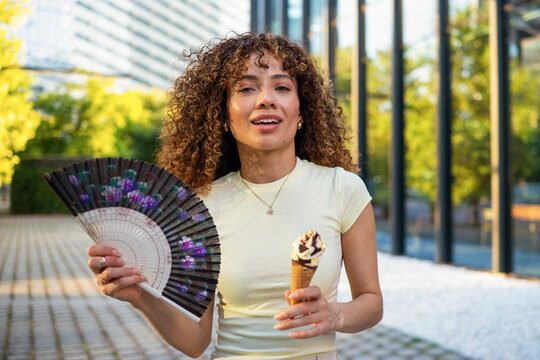 Young woman cooling off with fan and ice cream