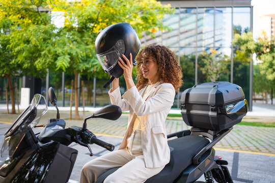 Woman with curly hair putting on helmet for scooter ride