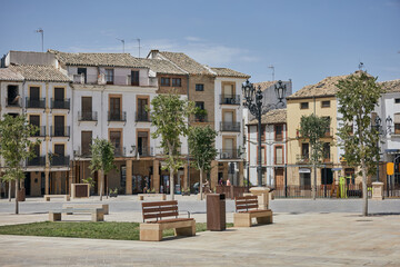 Open public square with traditional facades, balconies, tiled roofs, benches and ornamental street lamps in the historic center of Baeza, Andalusia, Spain © Goodwoon Mallorca