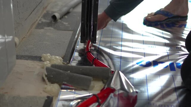 Highly engaging commercial ready closeup video of a worker installing red floor heating pipes using a professional tacker tool.