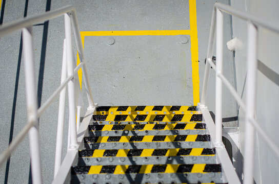 Access stairway on board a vessel fitted with high-visibility black-and-yellow anti-slip markings and protective handrails. The markings reduce the risk of slip, trip and falls