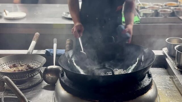 Chinese Street Food &ndash; Stir Frying Noodles in Large Wok Over Open Flame at Outdoor Market Stall