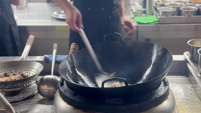 Chinese Street Food &ndash; Stir Frying Noodles in Large Wok Over Open Flame at Outdoor Market Stall