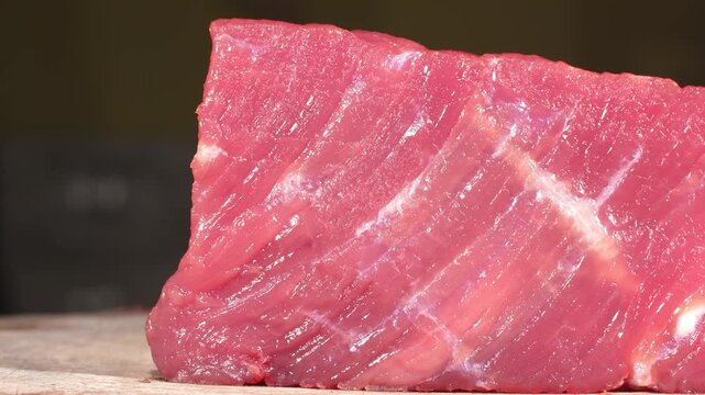Camera dolly passing close to fresh raw beef steak with diagonal meat grain on wooden board.
