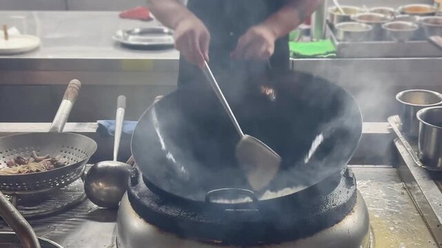 Chinese Street Food &ndash; Stir Frying Noodles in Large Wok Over Open Flame at Outdoor Market Stall