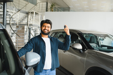 Happy indian man holding new car keys in showroom