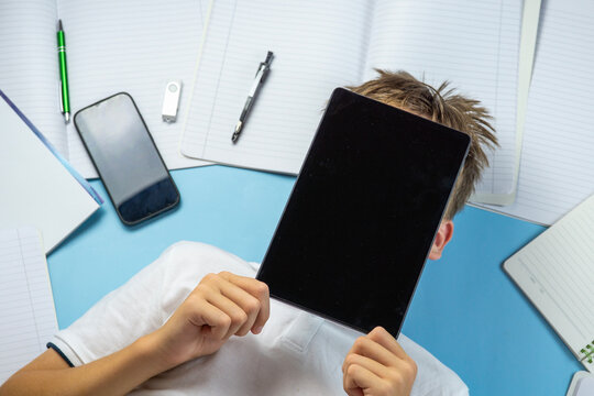school student tablet screen black covering face holding device laying down blue background with notebooks and smartphone with copy space for banner design concept of education technology e-learning