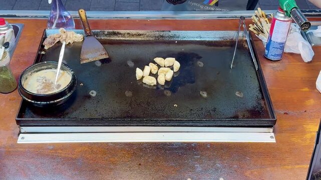 Korean Street Food,Myeong Dong  &ndash; Frying Potato Slices with Red Chili Pepper on Hot Griddle at Outdoor Market