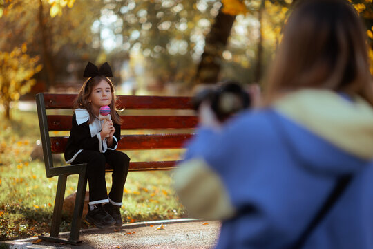 Mother Taking Autumn School Portrait of Her Little Girl on a Park Bench. Loving mom captures beautiful outdoor portraits of her daughter wearing elegant trousers