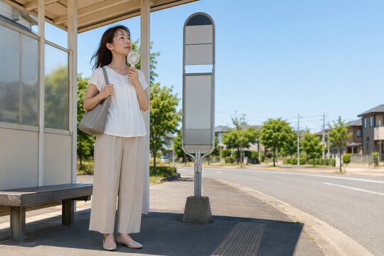 真夏のバス停でハンディファンを使う女性