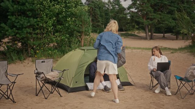 Multiethnic young adults camping on beach, Caucasian woman folding sleeping bag and Black man carrying cooler. Ideal for outdoor recreation and travel lifestyle promotional campaigns