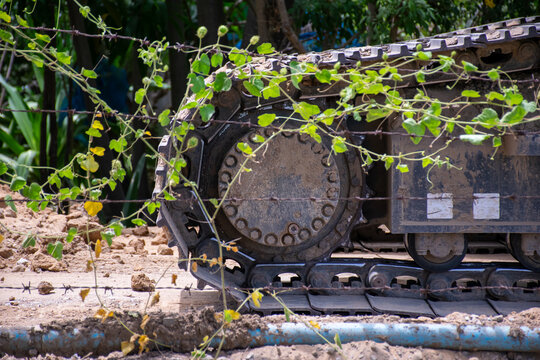 Close up of muddy excavator crawler track behind barbed wire climbing vines showing heavy machinery construction equipment engineering industrial work site details