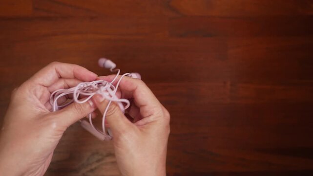 Top view of woman hands on left side trying to untangle headphone cable on wooden desk with copy space, giving up in frustration, obstacle concept.⁠