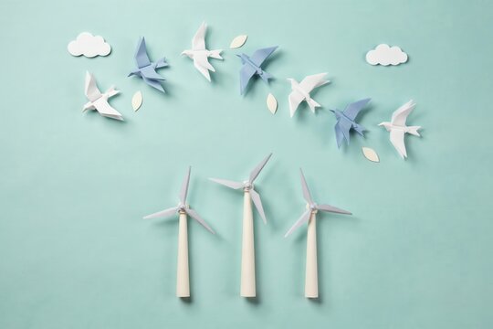 Origami paper wind turbines and flying birds on blue background representing green renewable energy and eco friendly concept