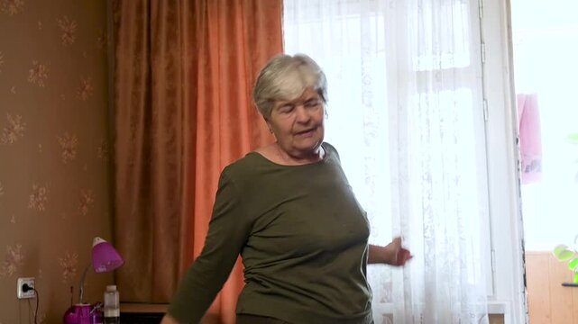 Active Elderly Woman Doing Morning Gymnastics and Stretching at Home by the Window