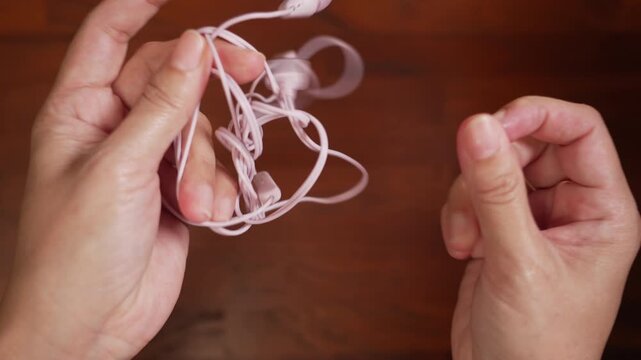 Centered top view of woman hands aggressively pulling tangled headphone wire on wooden desk, failing in frustration, stress concept.⁠