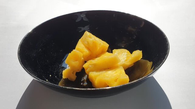 Pineapple slices served in a black bowl on a white background.