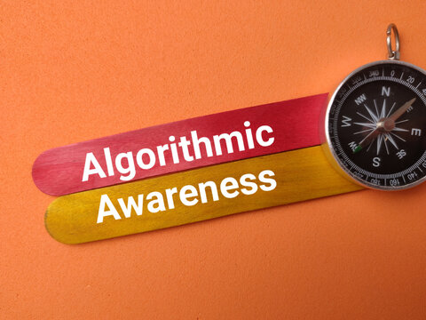 Red and yellow craft sticks labeled Algorithmic Awareness lie next to a compass on an orange surface