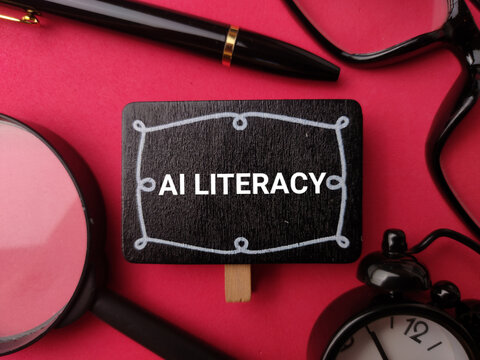 A small blackboard labeled AI LITERACY rests among a magnifying glass, pen, clock, and glasses on red