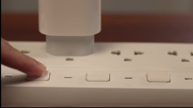 Close up on left side with copy space and slow zoom in of woman hand repeatedly pressing stuck switch on power strip on wooden desk, flickering red light until on, solution concept.