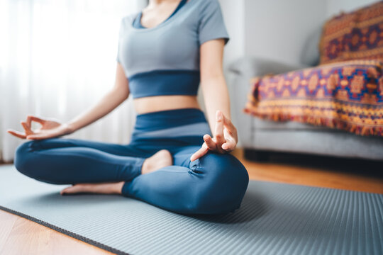 Young adult asian woman in sportswear exercise yoga, pilates, meditation and stretching on a mat peaceful lifestyle routine at home