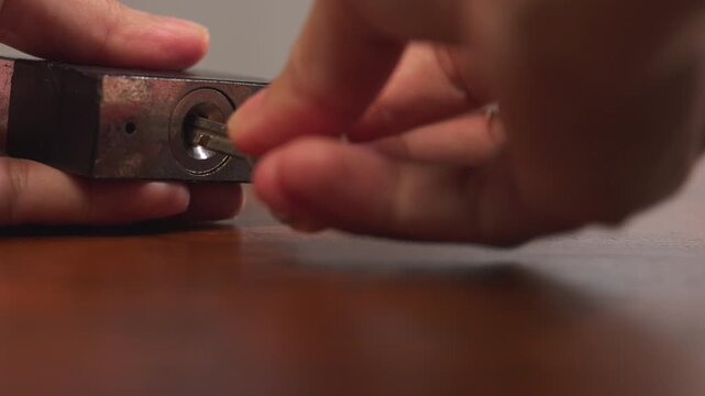 Close up of woman hands picking up key, inserting into padlock on wooden table, twisting repeatedly, trial and error concept.⁠