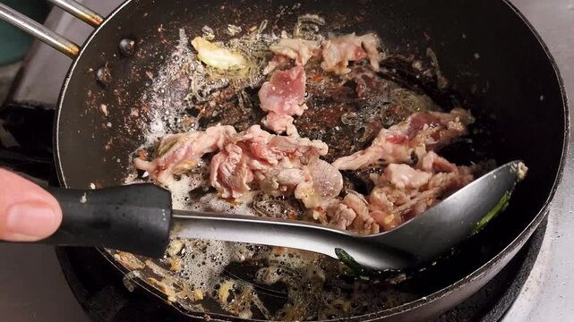 A close-up shot of raw pork slices being actively stirred and cooked with garlic in a hot frying pan, showing bubbling oil and steam. Perfect for culinary, cooking, and Asian food concepts.